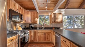 A modern kitchen with wooden cabinets, a stainless steel stove, and a large window with a view of trees. - Spacious, newly remodeled, perfect location w/BBQ, Hot Tub, pool table, SmartTV (Carnelian Bay)