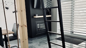 Un interior moderno con una mecedora de madera, una escalera negra y un ventanal con persianas.