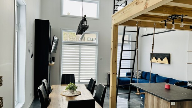 Un interior moderno con zona de comedor, un dormitorio estilo loft con escalera de madera y una cocina.