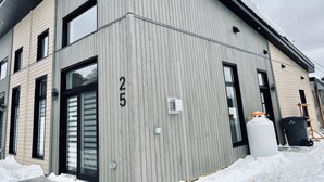 Un edificio moderno con fachada de madera gris, ventanas de marco negro y el número '25' exhibido en la pared.