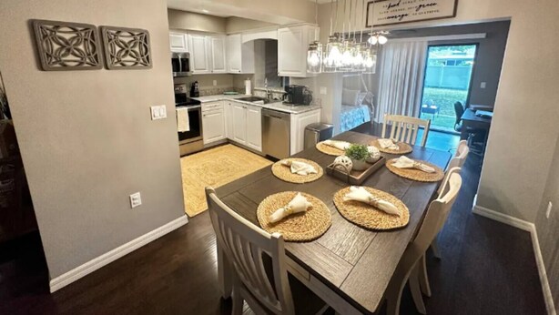 A modern kitchen with white cabinets, a dining area with a dark wooden table, and a chandelier. - A Peaceful Family Friendly Home in Sarasota Fla, Legacy Trail/Pinecraft (Sarasota)