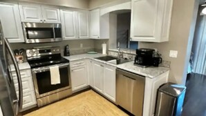A modern kitchen with white cabinets, stainless steel appliances, and a wooden floor. - A Peaceful Family Friendly Home in Sarasota Fla, Legacy Trail/Pinecraft (Sarasota)