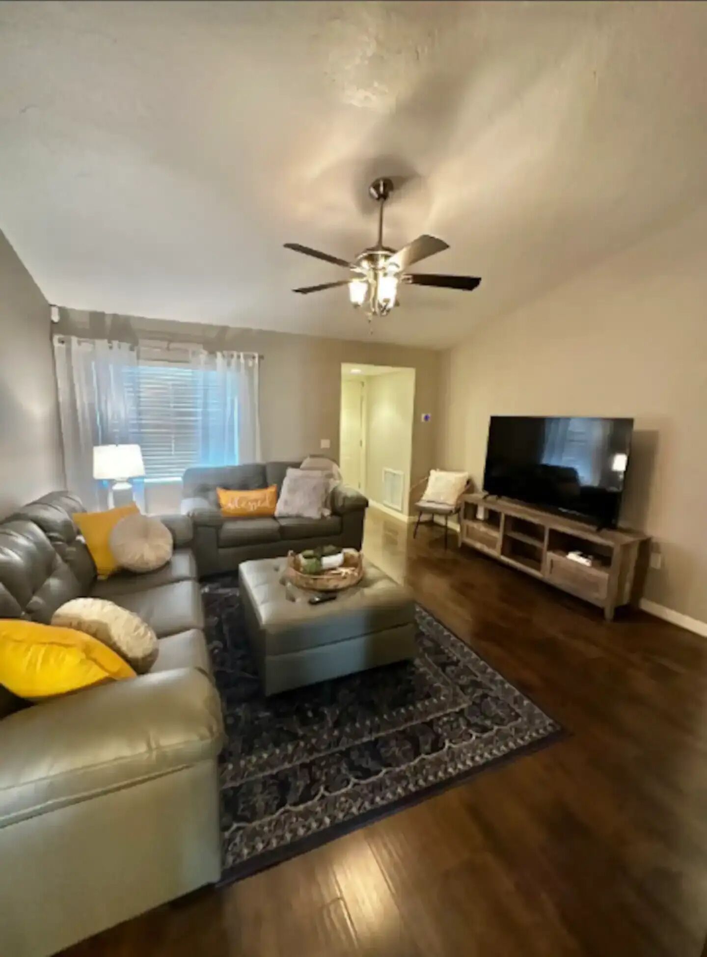 A living room with a grey sofa, ottoman, and a television on a wooden stand.