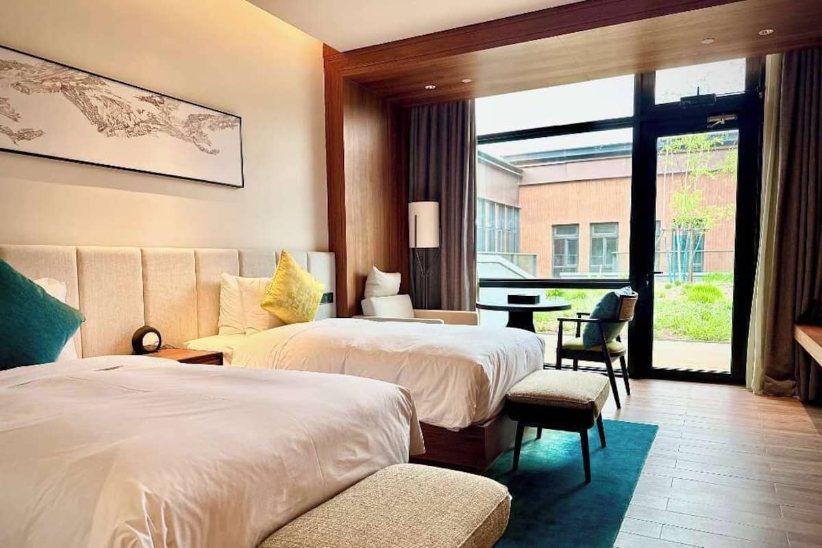 A hotel room with two beds, a desk, and a view of the outside.