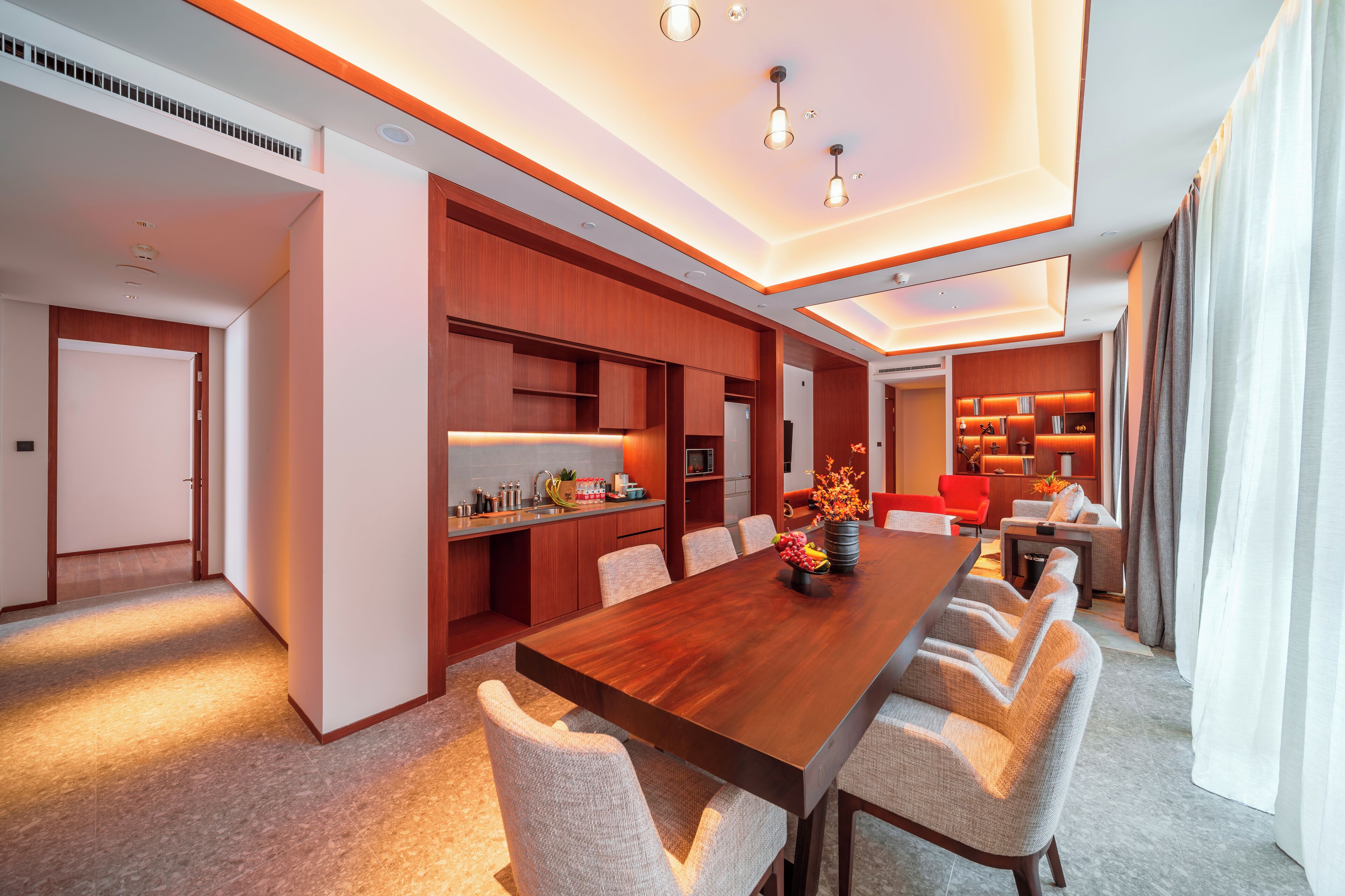 A modern kitchen with built-in appliances, a dining area with a long wooden table and multiple chairs, and a cozy seating area with a sofa and armchairs.