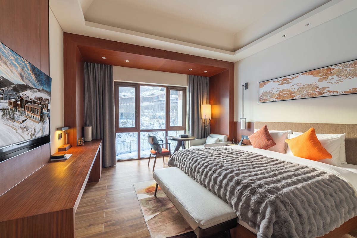 A hotel room with a large bed, a desk, a chair, and a view of the outdoors.