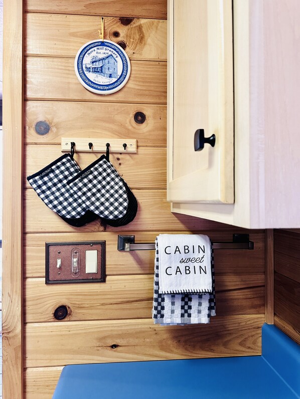 Un mueble de madera con un plato azul y blanco, una toalla a cuadros negros y blancos, y una toalla blanca con el texto 'CABIN sweet CABIN'.