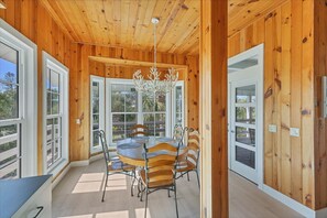 A wooden-paneled room with a round table and chairs, large windows, and a chandelier. - Timeless Coastal Island Retreat: 35 Palm (Placida)