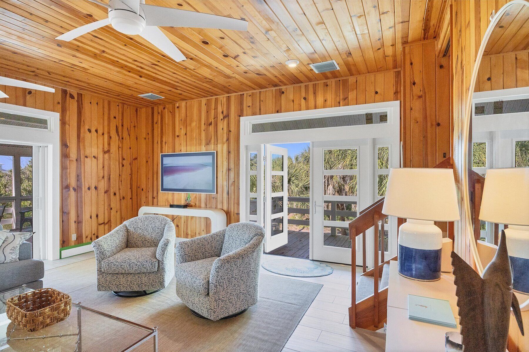 Un intérieur en bois avec deux fauteuils, un téléviseur et un ventilateur de plafond.