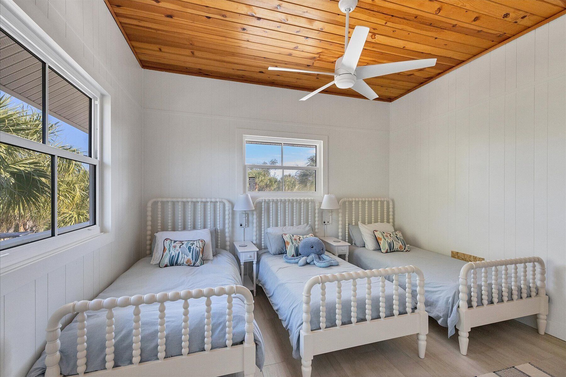 Un dormitorio con dos camas individuales, un ventilador de techo y una ventana con vistas a palmeras.