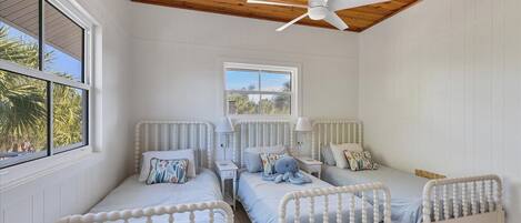 Un dormitorio con dos camas individuales, un ventilador de techo y una ventana con vistas a palmeras.