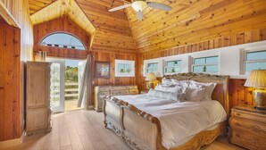 Ein Schlafzimmer in einer Holzhütte mit einem großen Bett, einem Deckenventilator und mehreren Fenstern.