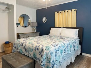 A bedroom with a bed, bedside table, lamp, mirror, and curtains.