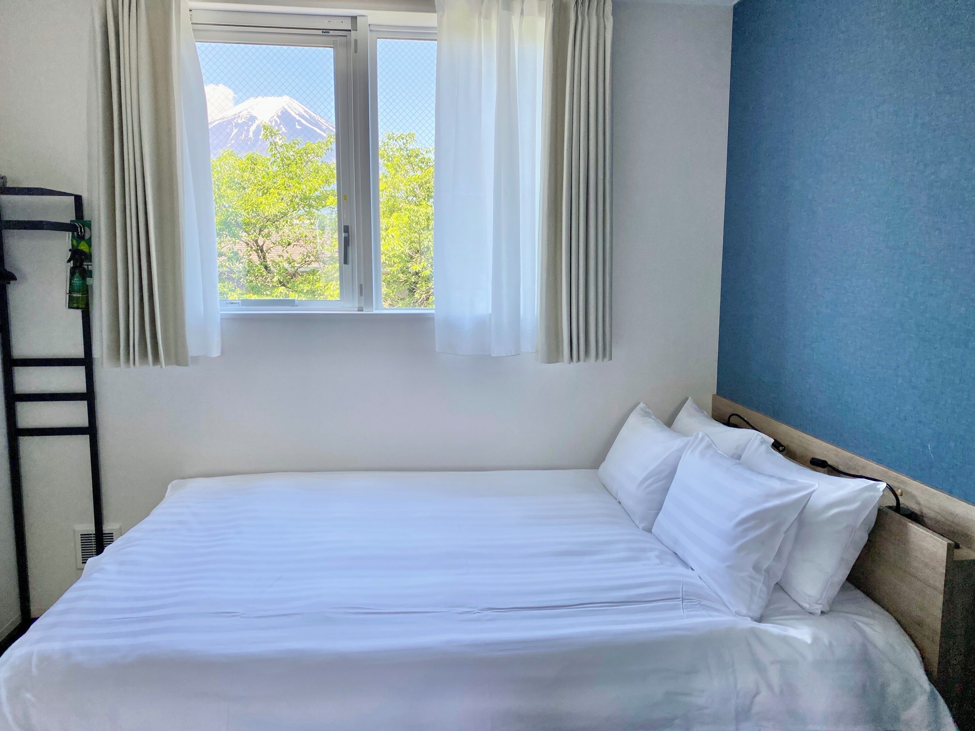 A hotel room with a bed, a window with curtains, a view of a mountain, and a blue wall.