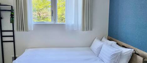 A hotel room with a bed, a window with curtains, a view of a mountain, and a blue wall.