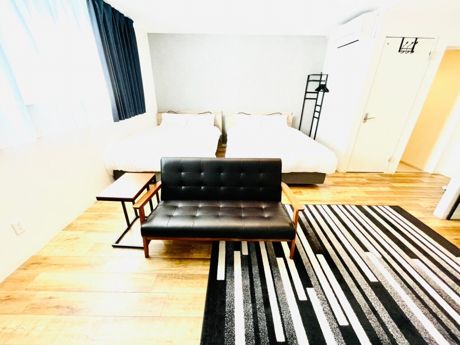A hotel room with a black leather sofa, a wooden coffee table, a striped rug, and two beds with white bedding.