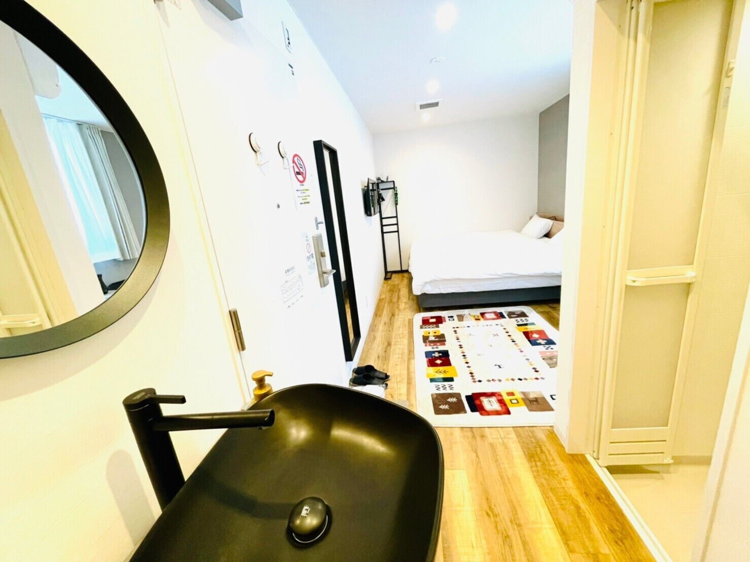 Una habitación de hotel compacta con un espejo redondo, un lavamanos pequeño, una cama con un tapete de colores y un armario.