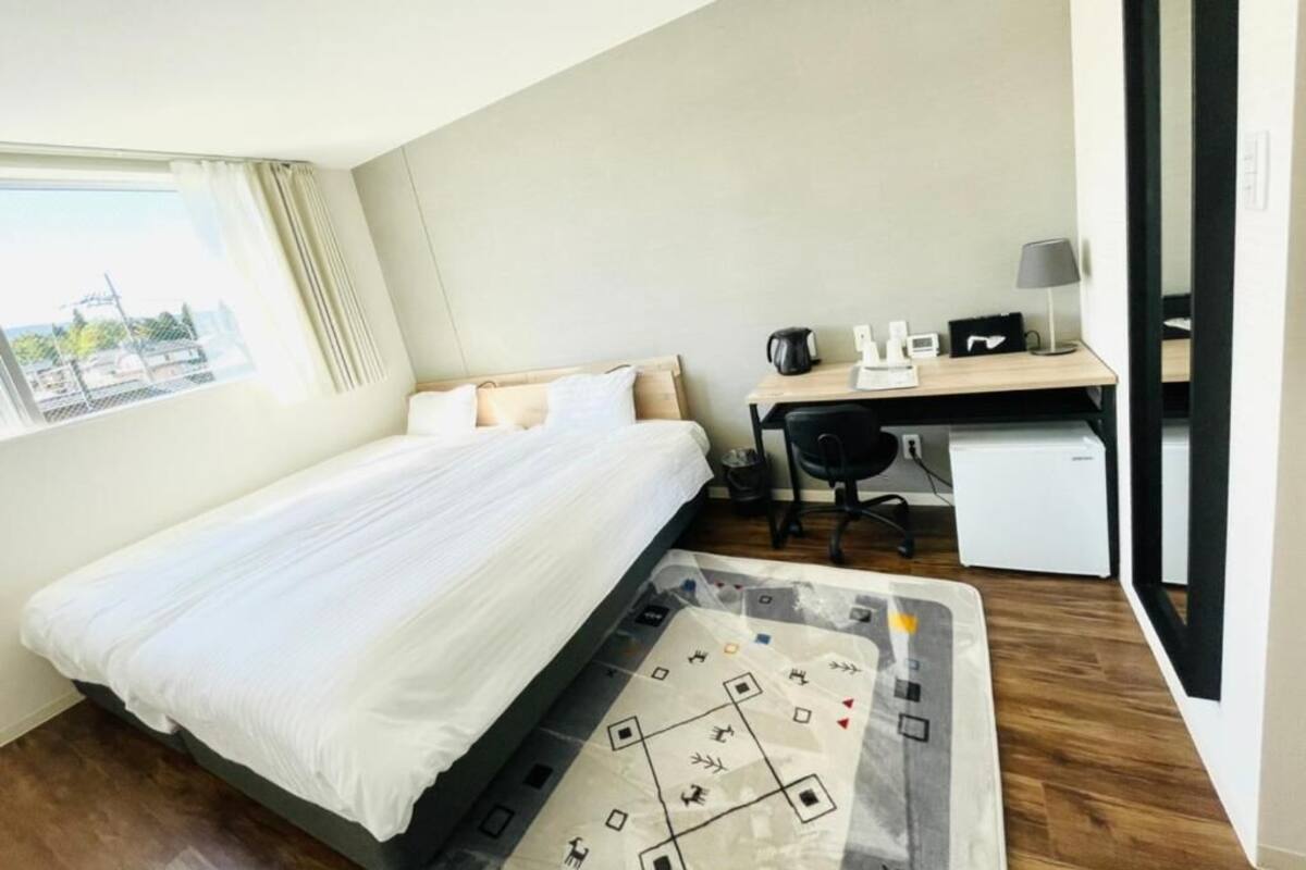 Habitación de hotel con cama, escritorio, silla y un refrigerador pequeño.