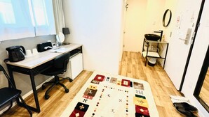 Une petite pièce bien éclairée, avec un plancher en bois, un bureau avec une chaise, une machine à café, une lampe et un climatiseur fixé au mur.