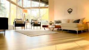 Un salon spacieux avec une grande fenêtre, un canapé blanc, une table basse et un lampadaire.