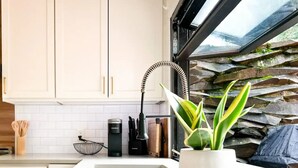 Une cuisine moderne avec des meubles blancs, un évier encastré et une fenêtre donnant sur un mur en pierre.