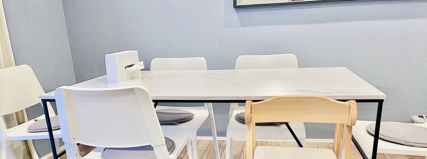 A conference room with a white marble table and white chairs, including one with a wooden backrest.