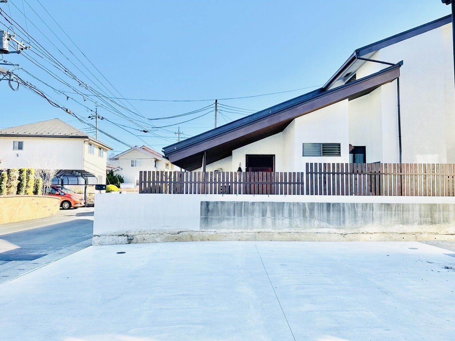 Un edificio residencial moderno con techo inclinado, pared de hormigón y valla de madera.