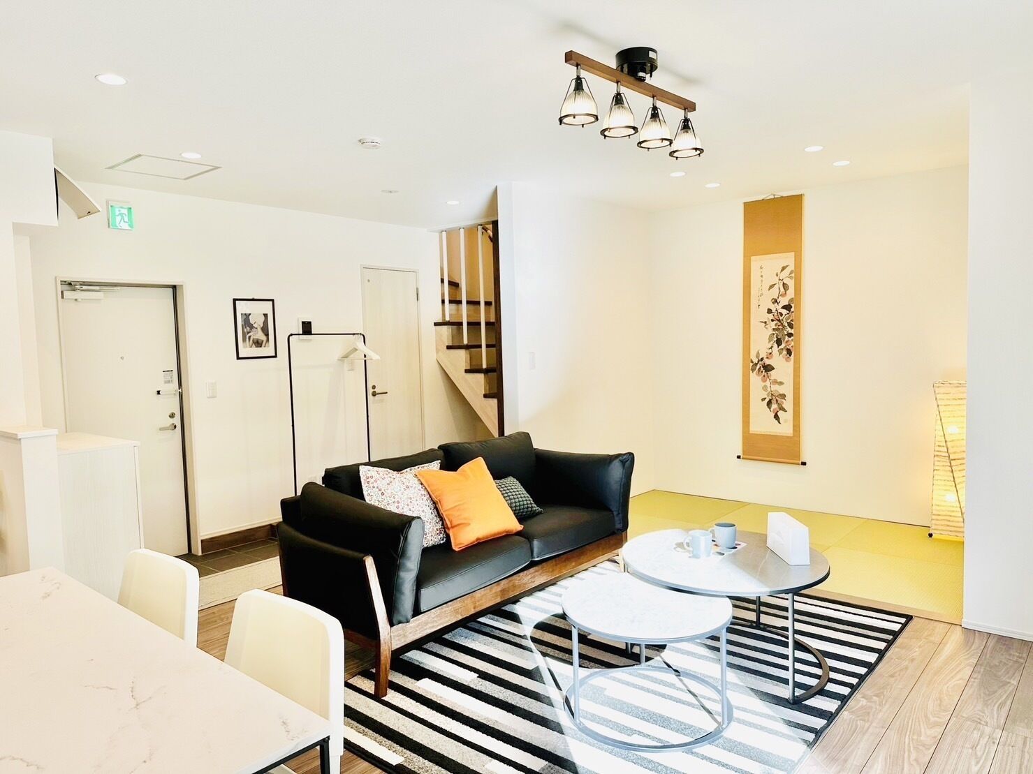 Quarto de hotel moderno com sofá de couro preto, mesa de centro redonda, tapete listrado e escada ao fundo.