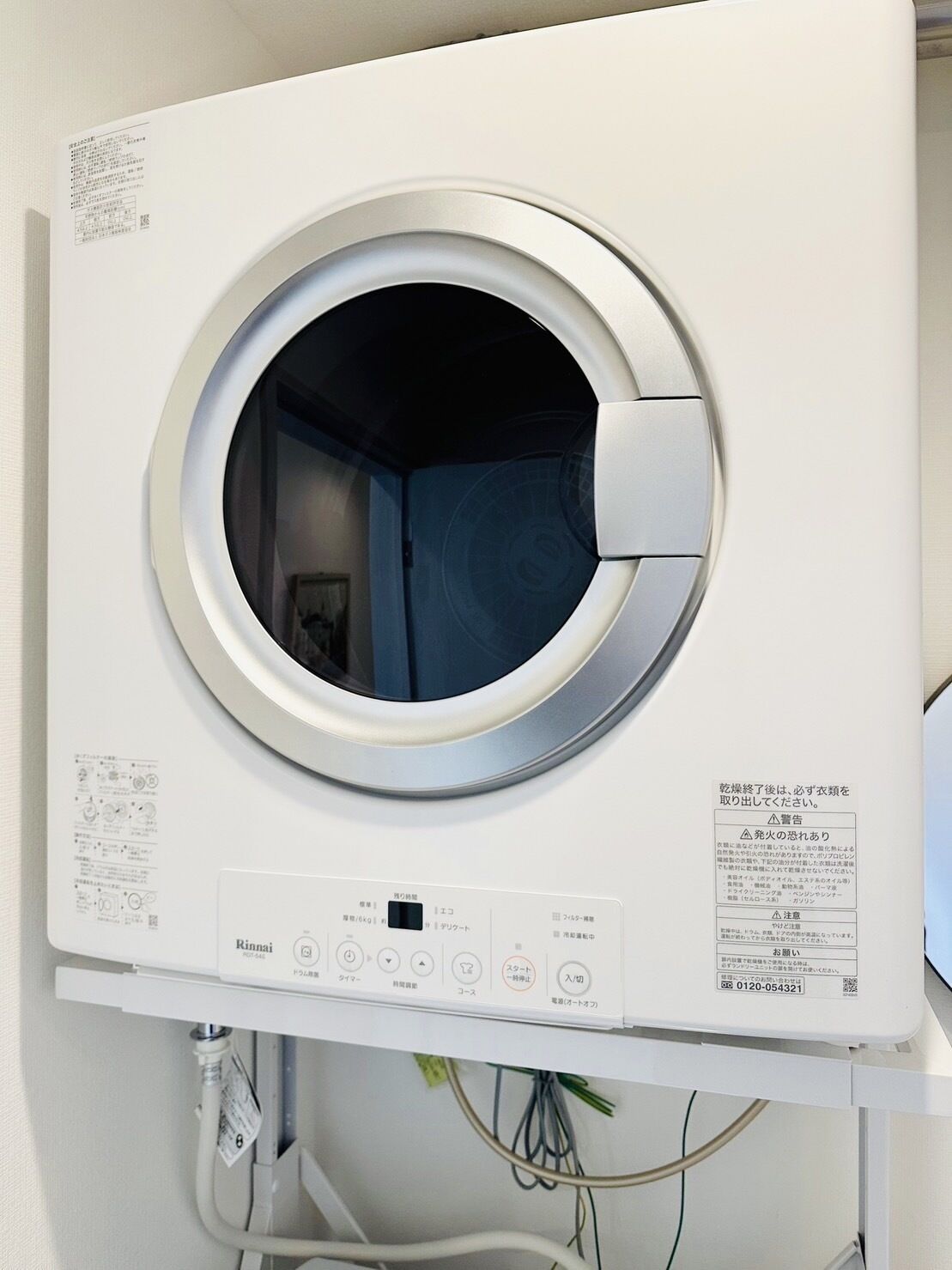 A front view of a white, wall-mounted washing machine with a control panel below.