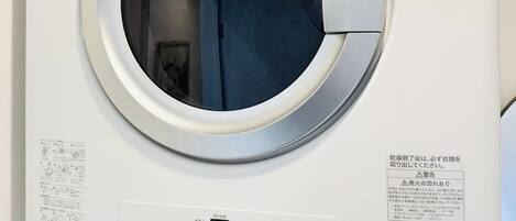 A front view of a white, wall-mounted washing machine with a control panel below.