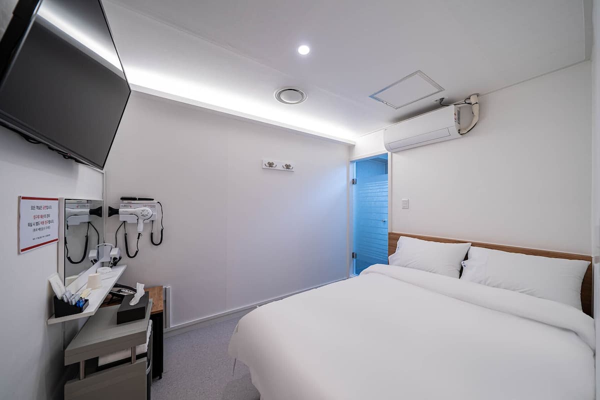 Habitació d'hotel amb llit, televisió penjada a la paret, escriptori amb mirall i assecador de cabells.