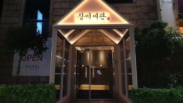 A building entrance with a sign in Korean and English, a glass door, and a small overhang above the door. - Rose Inn (Seoul)