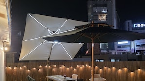 An outdoor patio with tables and chairs, a large umbrella, and a wooden fence. - Rose Inn (Seoul)