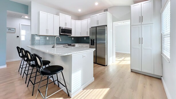 A modern kitchen with white cabinets, stainless steel appliances, and a central island with bar stools. - Gorgeous Downtown Sarasota, Historic Laurel Park Home. (Sarasota)