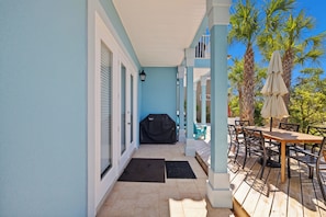 A covered patio with a wooden table and chairs, a grill, and palm trees in the background. - Coco's Cabana - Steps to Beach! (Panama City Beach)