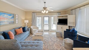 A spacious living room with a grey sofa, a white armchair, a coffee table, and a television on a wooden cabinet. - Coco's Cabana - Steps to Beach! (Panama City Beach)