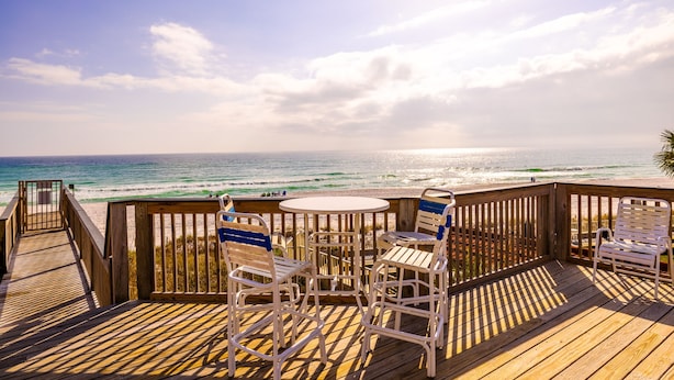 A wooden deck with a table and chairs overlooking a beach. - Coco's Cabana - Steps to Beach! (Panama City Beach)