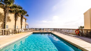 A swimming pool with clear blue water, surrounded by lounge chairs and palm trees. - Coco's Cabana - Steps to Beach! (Panama City Beach)