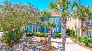 A residential area with a blue building, palm trees, and a paved walkway. - Coco's Cabana - Steps to Beach! (Panama City Beach)