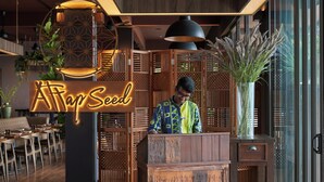 Uma área de recepção com uma mesa de madeira, um letreiro de neon com a inscrição "A Place Seed" e uma grande janela.