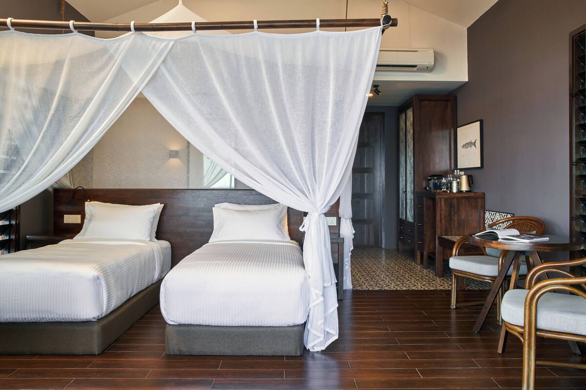 Habitación de hotel con dos camas, una cama con dosel, zona de comedor con sillas y una pequeña mesa.