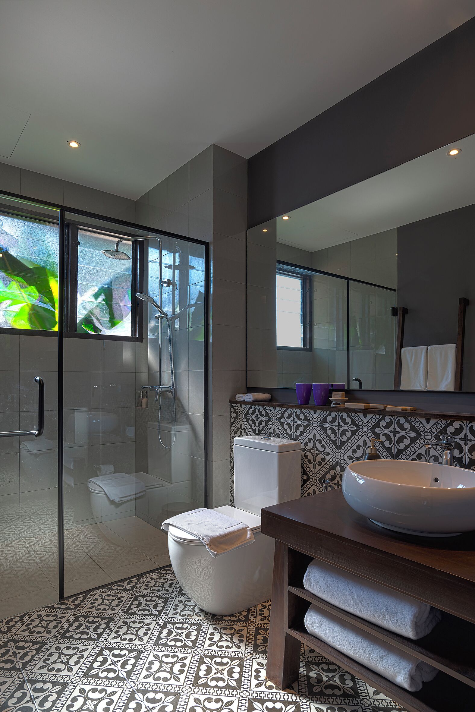 Un baño moderno con ducha de vidrio, un espejo grande y un lavamanos sobre encimera.