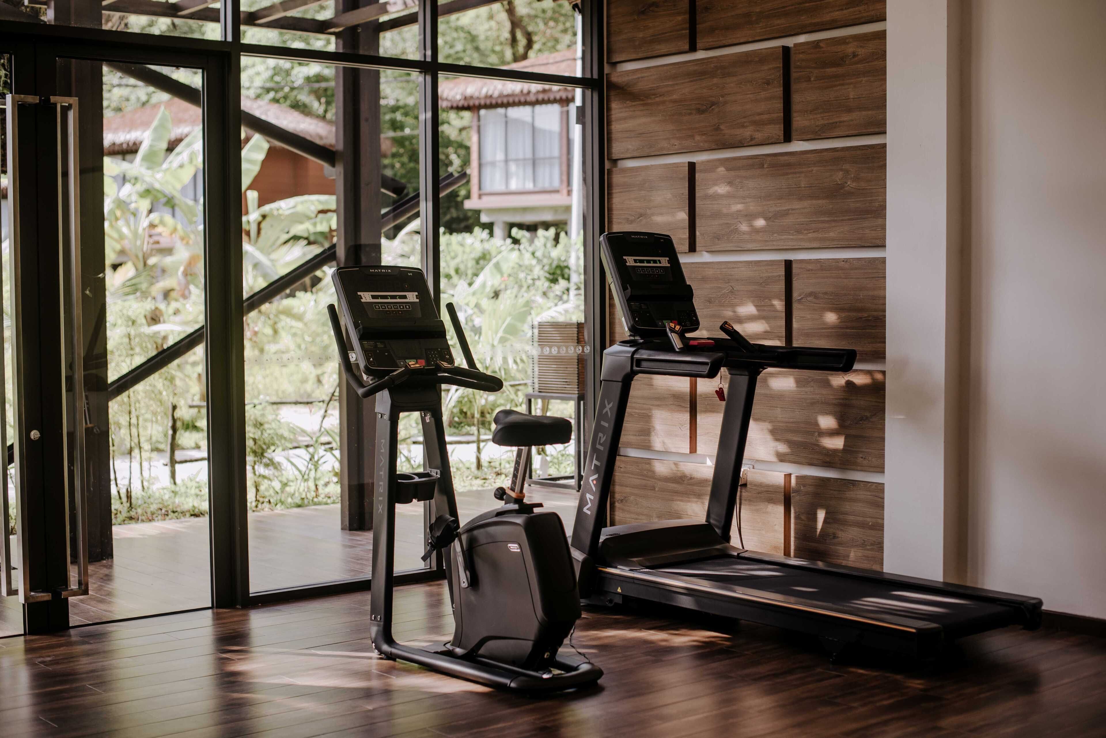 Un gimnasio con equipo de ejercicio, ventanas amplias y un muro de madera.
