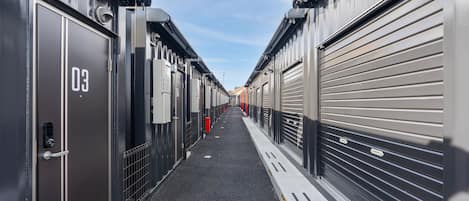 A corridor with closed metal doors, each marked with a number, leading to a row of garages.