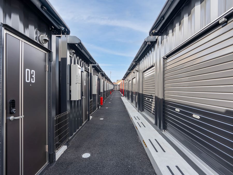 A corridor with closed metal doors, each marked with a number, leading to a row of garages.