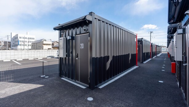 A row of compact, modern buildings with a metallic exterior, numbered 20, adjacent to a parking area with marked spaces. - HOTEL R9 The Yard Fujioka (Fujioka)