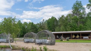 Outdoor seating areas with wicker chairs and sofas, a wooden building with a covered patio, and a natural setting with trees and a body of water.