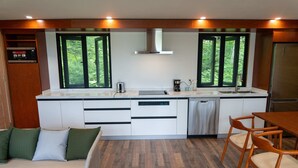 A modern kitchen with a built-in oven, a coffee maker, and a dishwasher. There are two windows with a view of greenery outside.