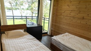 Een slaapkamer met twee bedden, een houten hoofdeinde, een nachtkastje en uitzicht op een meer door een groot raam.