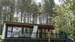 Eine moderne Hütte mit großen Fenstern, einer Holzdiele und einer Treppe, die zu einem überdachten Bereich führt.